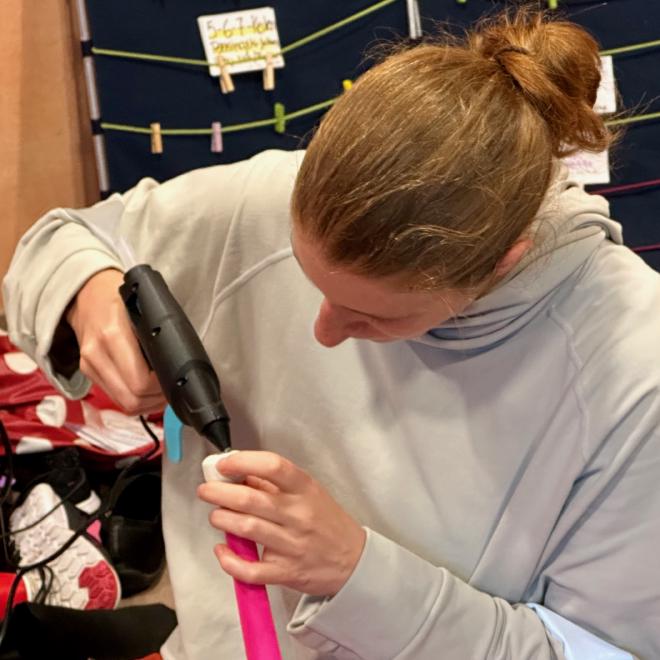 A woman uses a hot glue gun to cover the screw on the handle of a juggling club