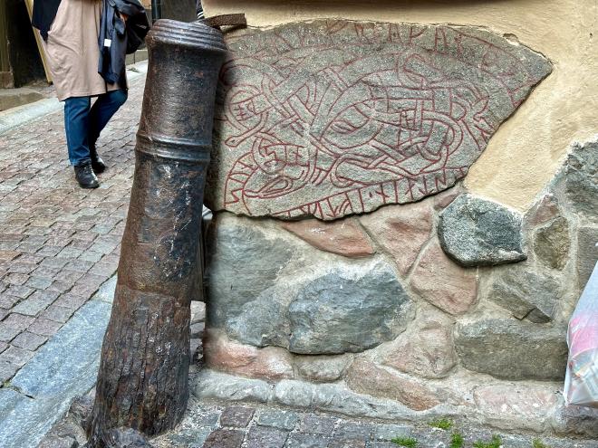 &ldquo;street corner with a cannon mounted vertically protecting a rune stone embedded in the building wall&rdquo;